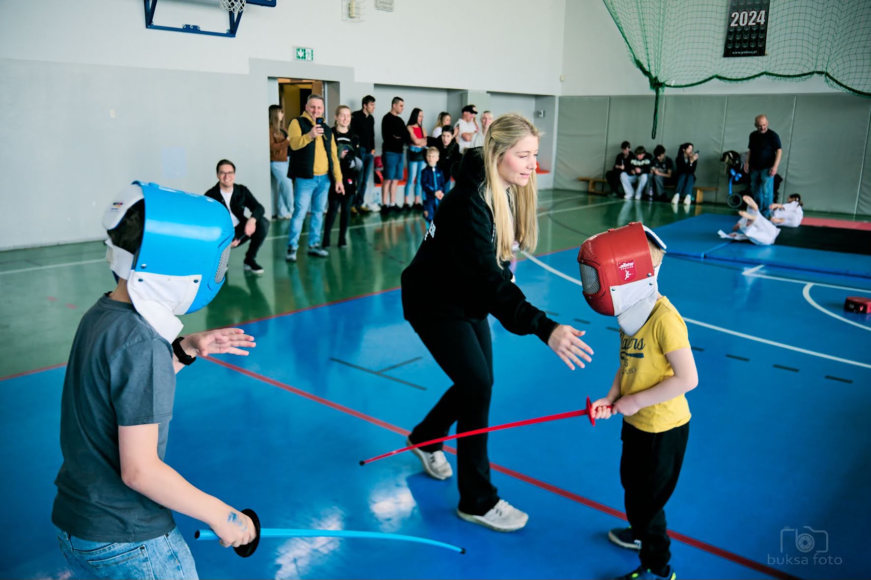 młodzi ludzie na macie trenują szermierkę