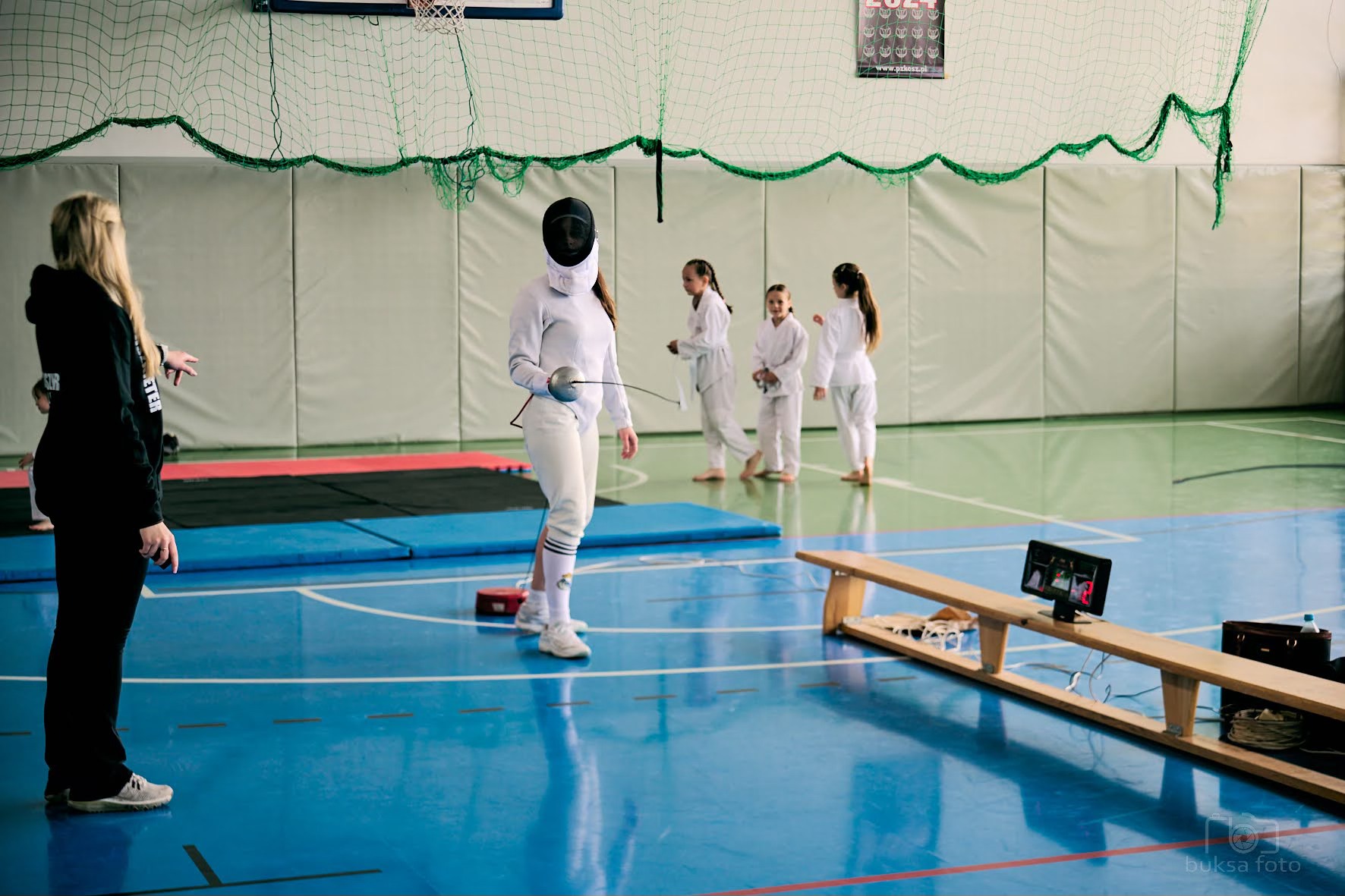 młodzi ludzie na macie trenują szermierkę