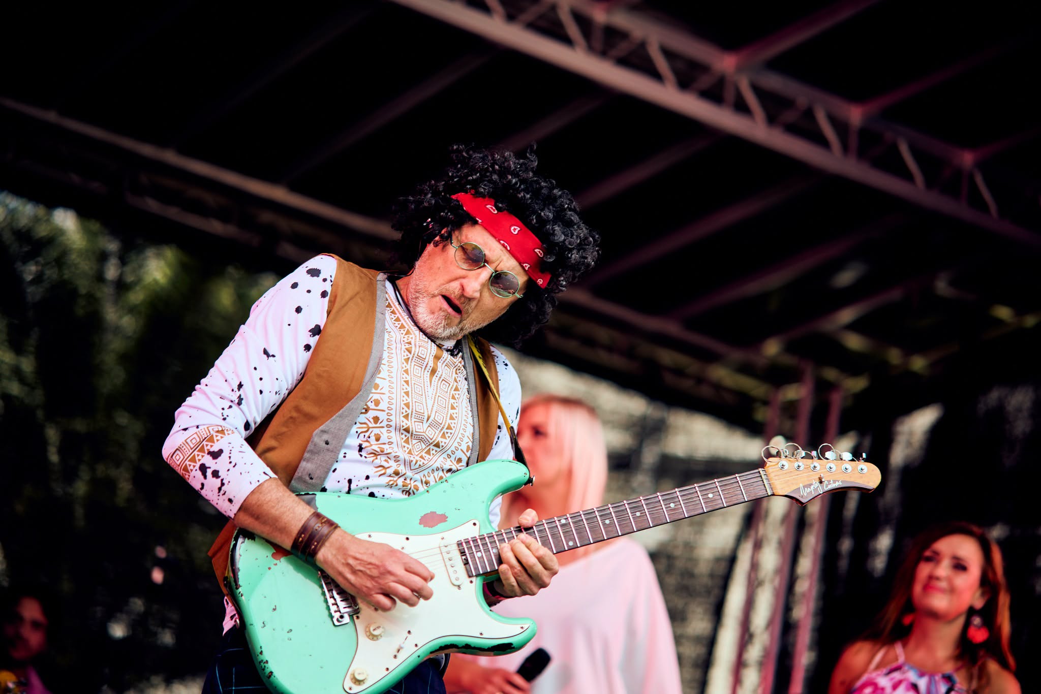 człowiek z czerwoną opaską na głowie stoi na scenie z gitarą