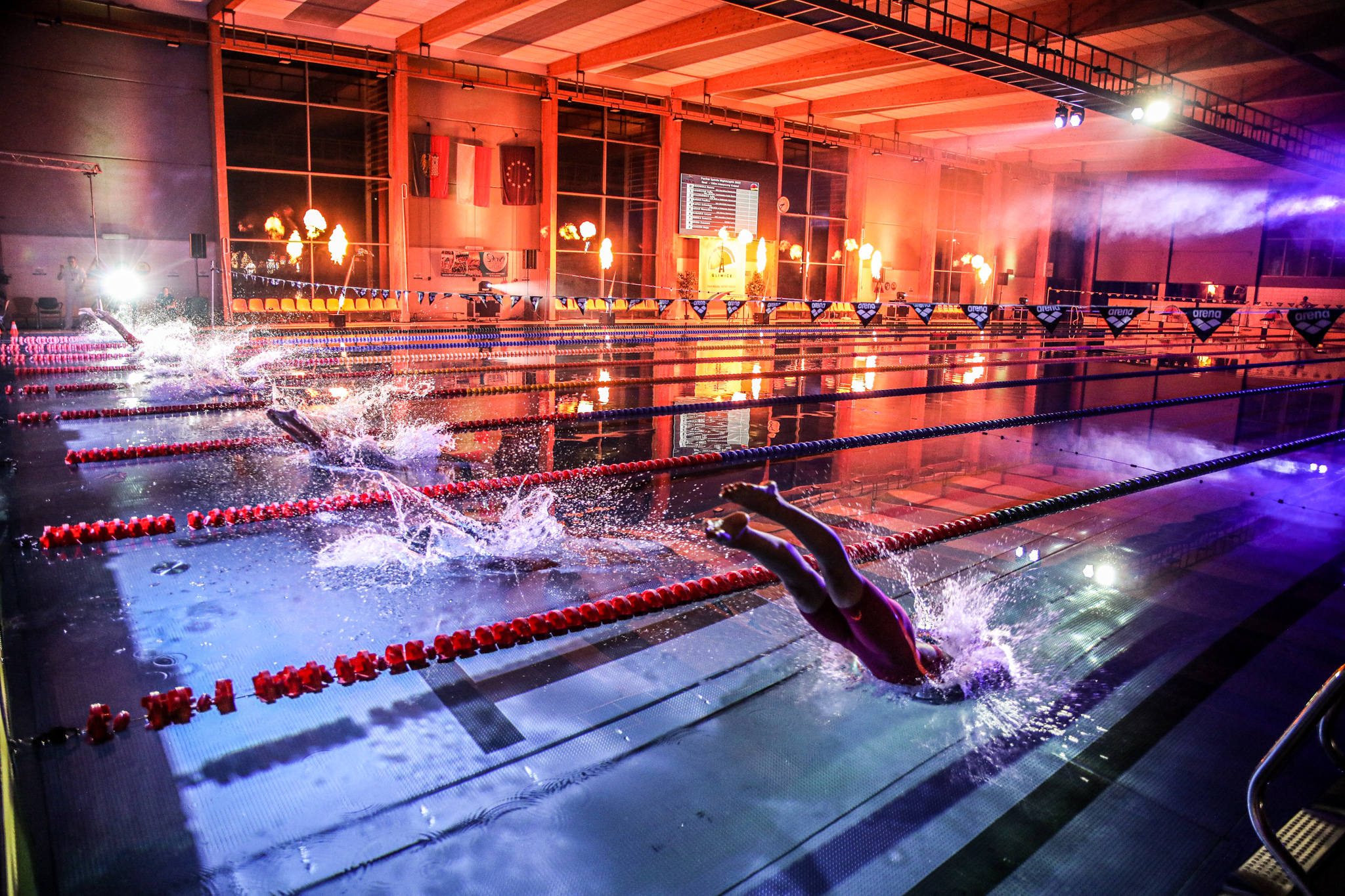 Pływacy wskakujący do basenu pośród kolorowych świateł