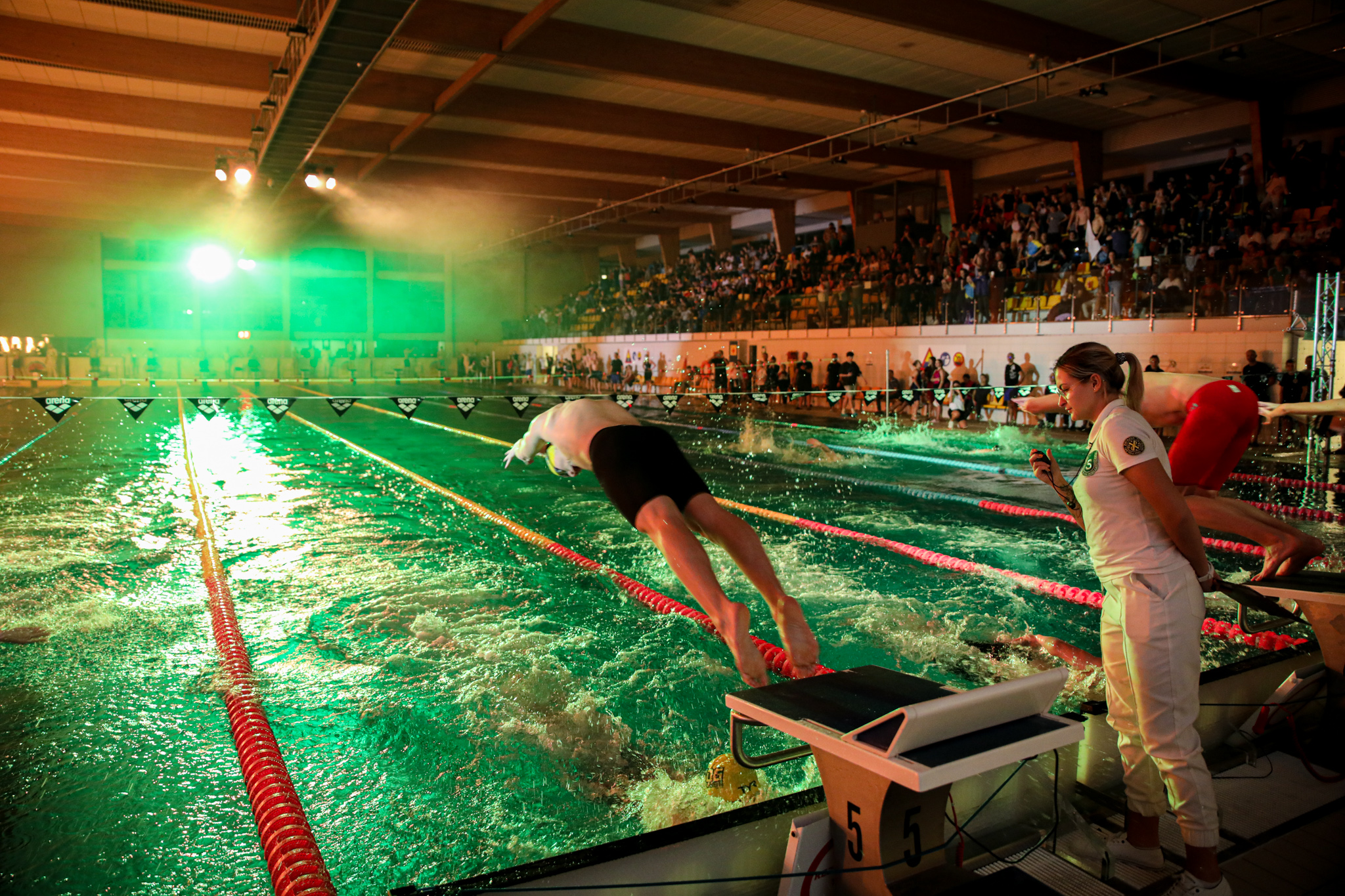 Pływacy wskakujący do basenu pośród kolorowych świateł