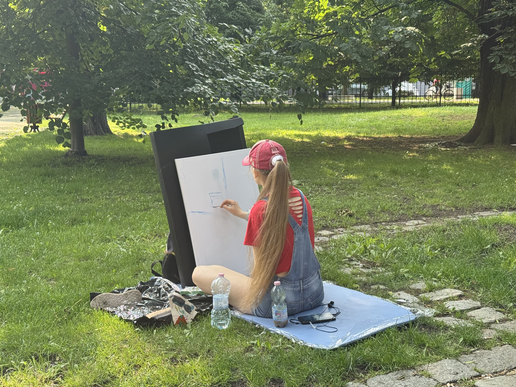 dziewczyna na trawie siedzi i maluje na sztaludze