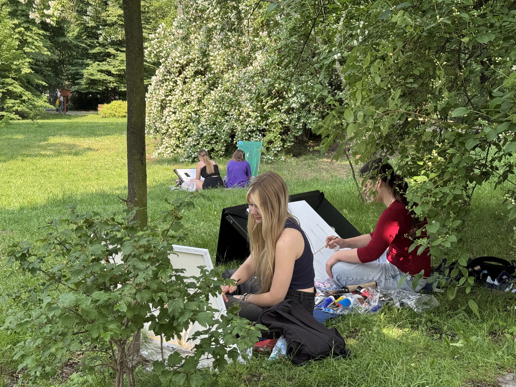 młodzi ludzie siedzą na trawie i malują na płótnach