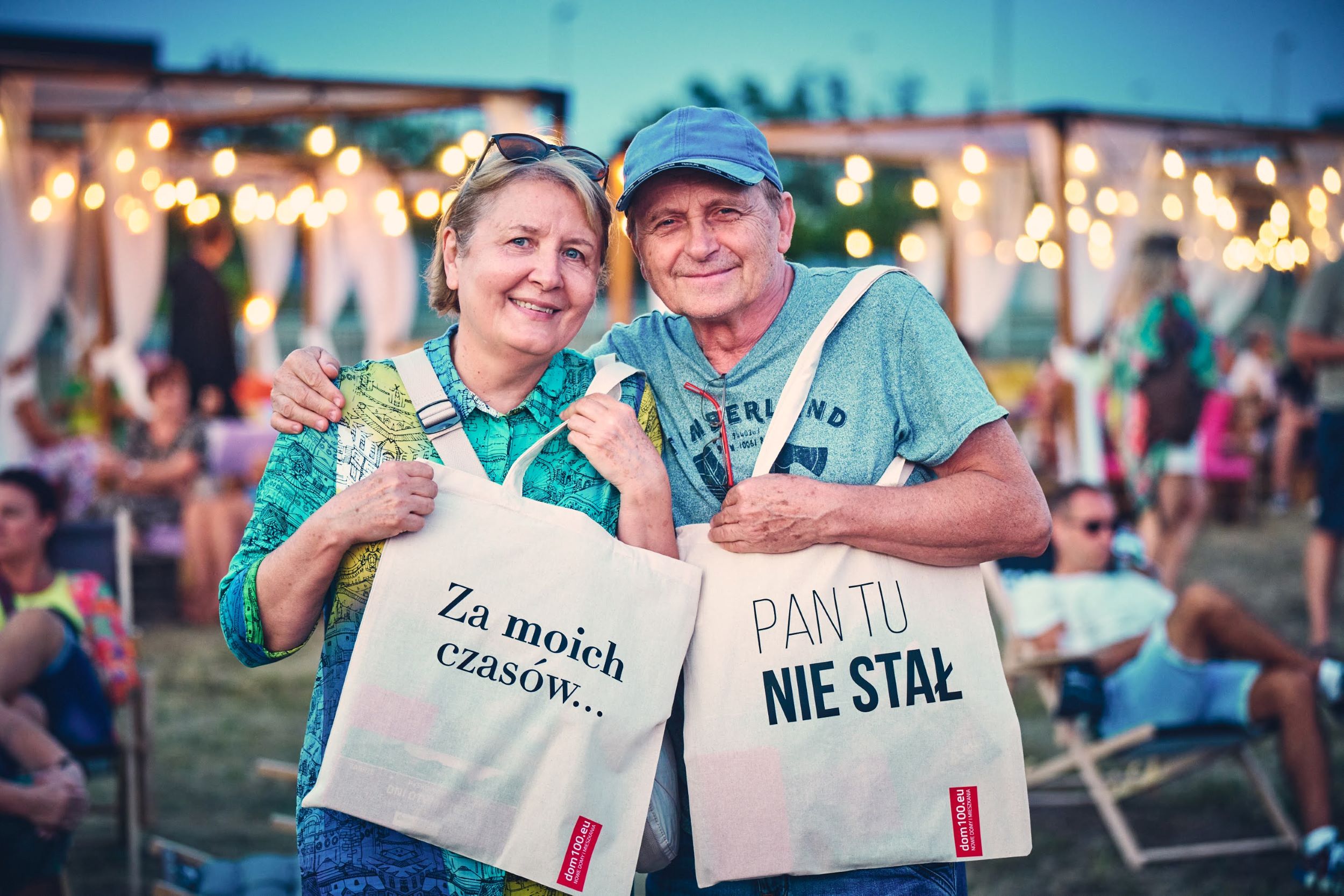 Uczestnicy festiwalu pozują do zdjęcia, pokazując torby