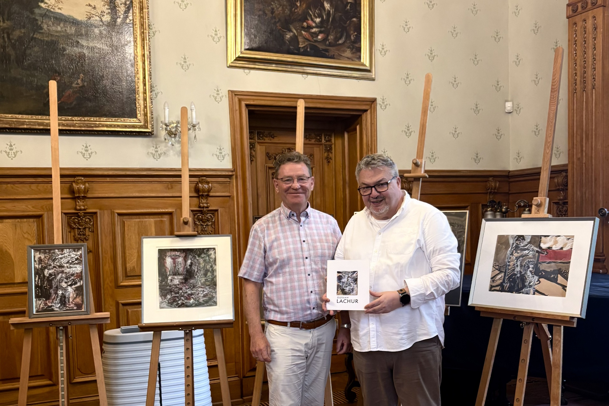Dwóch mężczyzn w Muzeum, jeden trzyma obraz, w tle obrazy na sztalugach